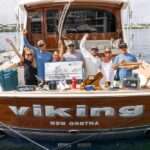 A sport-fishing team in the cockpit of their boat. Prizes and awards are arranged around them, and the middle anglers hold up an over-sized check.