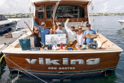 A sport-fishing team in the cockpit of their boat. Prizes and awards are arranged around them, and the middle anglers hold up an over-sized check.