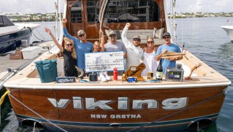 A sport-fishing team in the cockpit of their boat. Prizes and awards are arranged around them, and the middle anglers hold up an over-sized check.